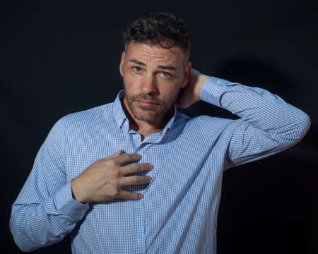 Man looking at camera. black studio background. Man 35 to 40 years old with dark hair touches his...