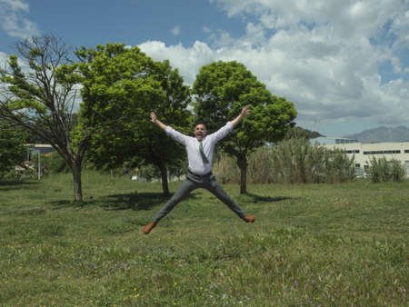 businessman jumping, in a park with green trees and has a winning, happy expression, jumping highの写真素材