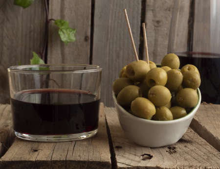 glass of wine with wine, with a lid of olives with chopsticks, on a wooden background and a bottle of wine out of focus. concept of having an aperitif.の写真素材