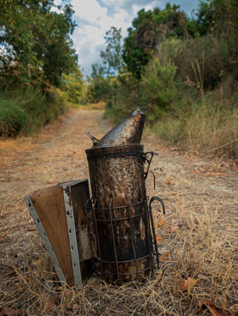 old and used bee smoker lying on the ground with a natural background of a road with trees, bushes and blue sky.の写真素材