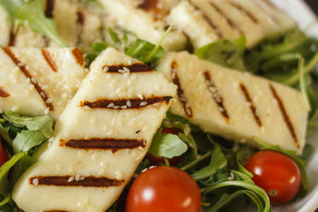 Traditional greek fried halloumi cheese on a white plate with herbs and cherry tomatoes. View from...
