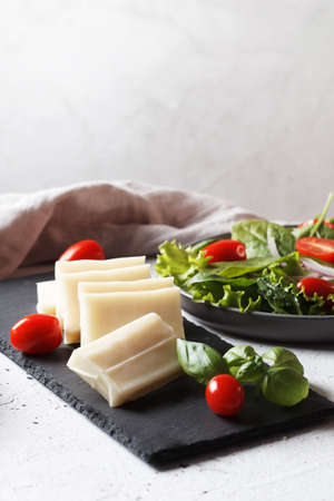 A piece of fresh sliced halloumi on a slate board with cherry tomatoes and spinach leaves. Preparing...