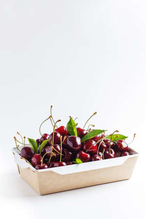 Fresh, ripe cherries in a cardboard box on a white background. copy space