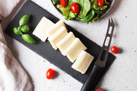A piece of fresh sliced halloumi on a slate board with cherry tomatoes and spinach leaves. Preparing to cook cheese on the grill. top viewの写真素材