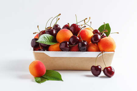 Apricots and cherries in paper packaging on a white background. the concept of eco-friendly packaging without plastic.の写真素材