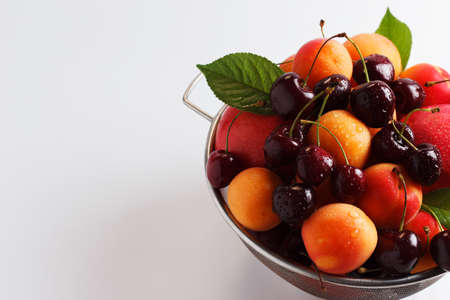 apricots and cherries in a metal bowl on a white background. copy spaceの写真素材