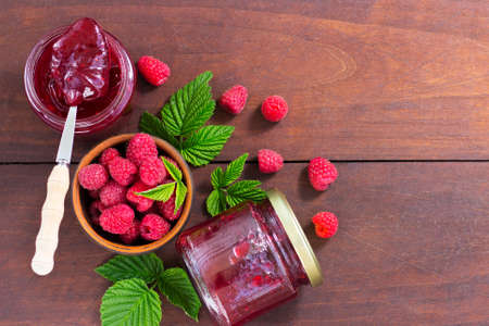 fresh raspberry jam in a glass jar on a wooden table, next to fresh raspberries. concept of homemade...
