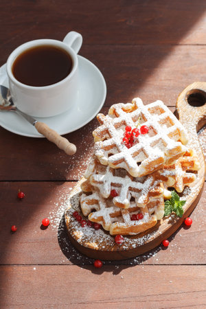 Waffles with berries sprinkled with powder. With a cup of tea on a wooden background. vertical photoの写真素材
