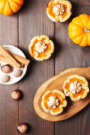 Pumpkin mini pies with whipped cream and spices on a wooden background. vertical photoの写真素材