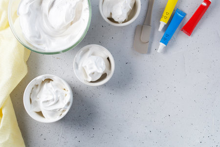 Whipped egg whites - meringue prepared for coloring in different colors, food coloring on a gray background. copy spaceの写真素材