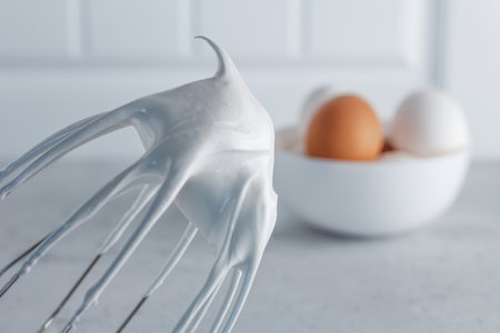 Whisked egg whites - whipped Italian meringue on a wire whisk and eggs on a gray background. copyspace.の写真素材