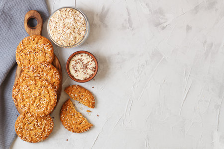 Oatmeal cookies with sesame seeds and flax seeds on a gray background with a jar of oatmeal and textiles. copy spaceの写真素材