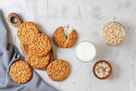 Oatmeal cookies with sesame seeds and flax seeds on a gray background with a jar of oatmeal and a glass of milk.の写真素材