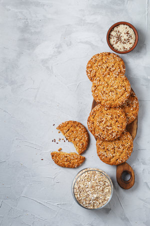 Oatmeal cookies with sesame seeds and flax seeds on a gray background with a jar of oatmeal and textiles. copy spaceの写真素材