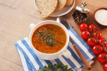 Vegetable soup with potatoes, cabbage, carrots and onions in a white bowl on the kitchen table. Vegetarian food.の写真素材