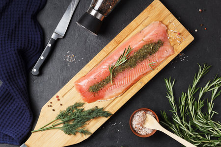 Salted fish fillet with spices and herbs:dill and rosemary on a wooden board on a black background.の写真素材