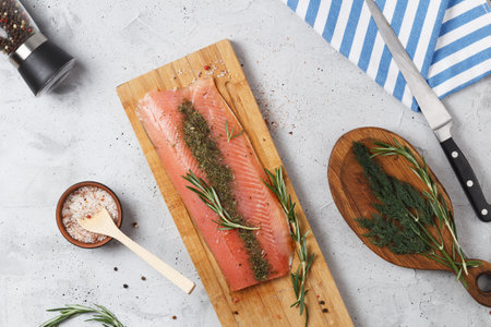 Salted fish fillet with spices and herbs: dill and rosemary on a wooden board on a gray background.の写真素材
