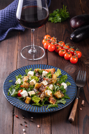 Salad with fried eggplant, herbs.tomatoes and feta cheese on a wooden background with a glass of red wine.の写真素材