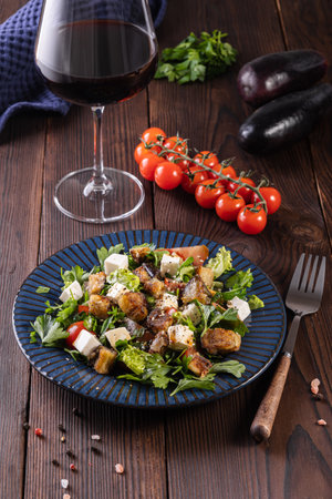 Salad with fried eggplant, herbs.tomatoes and feta cheese on a wooden background with a glass of red wine.の写真素材