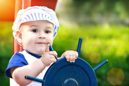 Little boy dressed up as a sailor holding the steering wheel in park.sunnyの写真素材