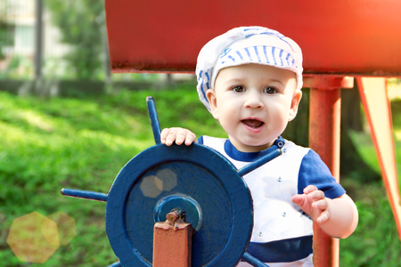 Little boy dressed up as a sailor holding the steering wheel in park.sunnyの写真素材