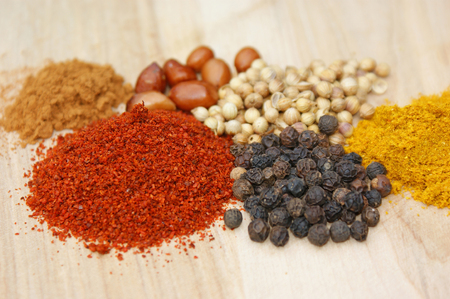 spicies on a wooden plate: chilli, pepper, coriander, curry, cinnamon, nutsの写真素材