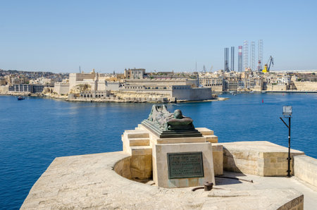 View of the War sculpture by Michael Sandle from the Siege Bell War Memorial or Malta Siege Memorial at the entrance to the Grand Harbor in Valletta, toward Fort St. Angelo and Birgu, an old fortified city in the South Eastern Region of Malta.のeditorial素材