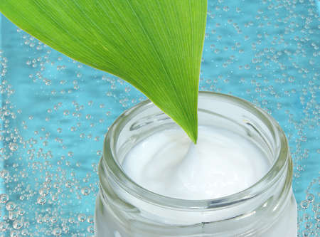cosmetic cream in a glass jar with green leaf on a blue water backgroundの写真素材