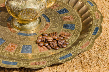 Small heap of coffee beans on an engraved (embossed) plate with an engraved metallic coffeepot, designed specifically for making Arabic coffeeの写真素材