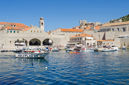 Dubrovnik, Croatia - June 9, 2017: The Old Harbor at Dubrovnik with the walls of the Old City, one of the most prominent tourist destinations in the Mediterranean Sea, filled with tourists and boats of all sorts.のeditorial素材
