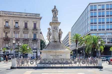Catania, Italy - July 3, 2017: Stesichorus Square and Bellini's Monument in the city center of the capital of Sicily with palm trees and Banco of Sicily to the right.のeditorial素材