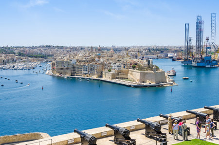Senglea, Malta - June 4, 2017:  Senglea peninsula as seen from the Upper Barrakka Gardens with its waterfront the St.Philip's Chapel dome, bastions of Fort Saint Michael and Saluting Battery with the guard showing a cannon to the touristsのeditorial素材
