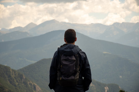 Young man with a backpack is wearing a dark raincoat and he's enjoying an amazing mountain views in Andorra.の写真素材