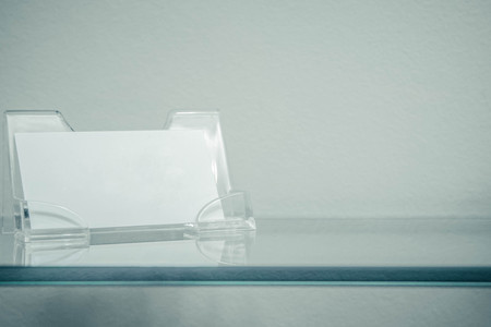 Acrylic paper stand for a blank card, business card stand on glass shelf isolated. Flyer leaflet white paper card template design.の写真素材