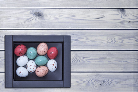 Colorful easter eggs in a brown box on a white wooden table, Easter concept with space for text. Top view.の写真素材