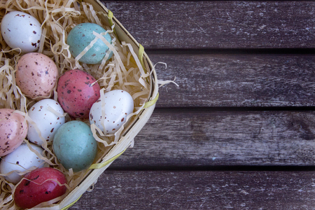 Multicolored easter eggs in a basket on a brown wooden table, Easter concept with space for text.の写真素材