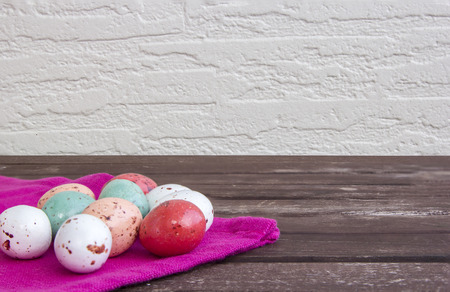 Colorful Easter eggs on a pink napkin / tablecloth on a brown wooden table and white wall.の写真素材