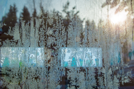 Ice patterns on windows with reflection of sunset in forest. Frozen snowflakes, crystal of ice.の写真素材