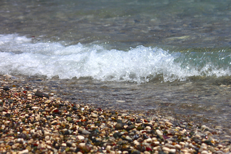 Bright colorful stones on the beach with clear clear water, foamy wave. Focus runs through the middleの写真素材