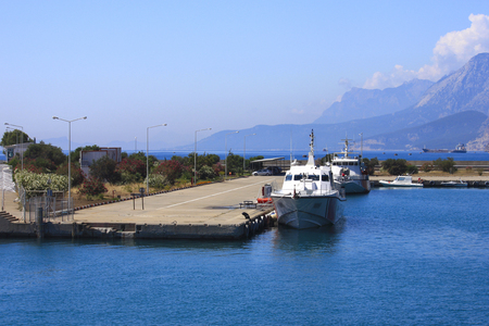 White ships at pier in small port, blue sky and mountains in background, Turkey.の写真素材