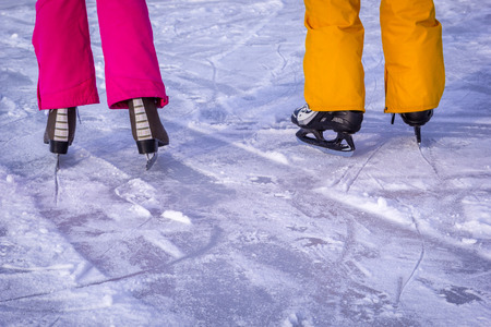Legs of teenagers girls, boys in bright pink yellow clothes in ice skates, closeup skating shoes in winter, healthy lifestyle.の写真素材