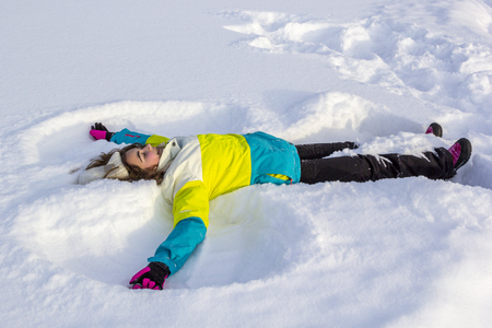 Cheerful and happy smiling cute girl lying on snow and making snow angel, flapping his arms and legs in different directions, enjoying and rejoicing winter.の写真素材