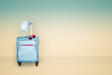 Light blue suitcase with a summer hat and fashionable  sunglasses on light beige and blue...