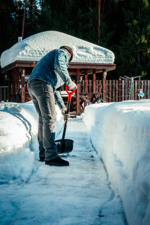 Man with shovel removing snow from sidewalk after snowstorm. Winter time in outdoors, clearing snow from backyard.の写真素材