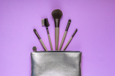 Silver cosmetic bag with makeup brushes on a pink background. Set of decorative accessories for woman. Top view, flat layの写真素材