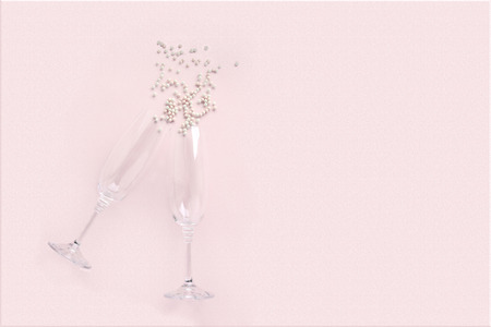 Champagne glasses with scattered white pearls on pink background. Celebrate party concept, minimal style. Greeting card for Christmas, birthday, wedding. Flat lay, top view.の写真素材