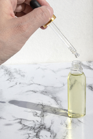 Pipette dropper with drop of natural oil above glass bottle on marble background. Natural organic skin care beauty products.の写真素材