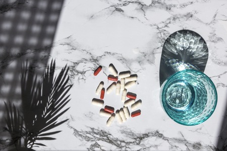 Blue glass of clean water and pills on white marble background with shadows from sunlight. Concept for pharmacy, medical dietic supplementsの写真素材
