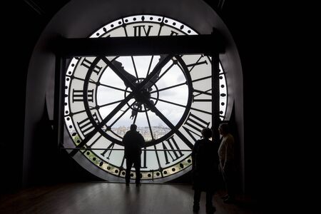 PARIS, FRANCE - MAY 9, 2019: Famous clock with roman numerals  and silhouette of man looking into round window in Orsay Museum, Paris, France.のeditorial素材