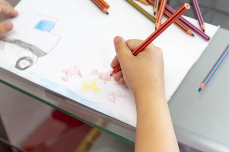 Child draws with colorful pencils. Children's drawing on theme of fishing with goldfish, car